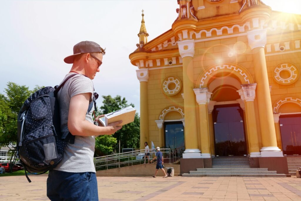 A young traveler examines a guidebook near a historic urban building on a sunny day.